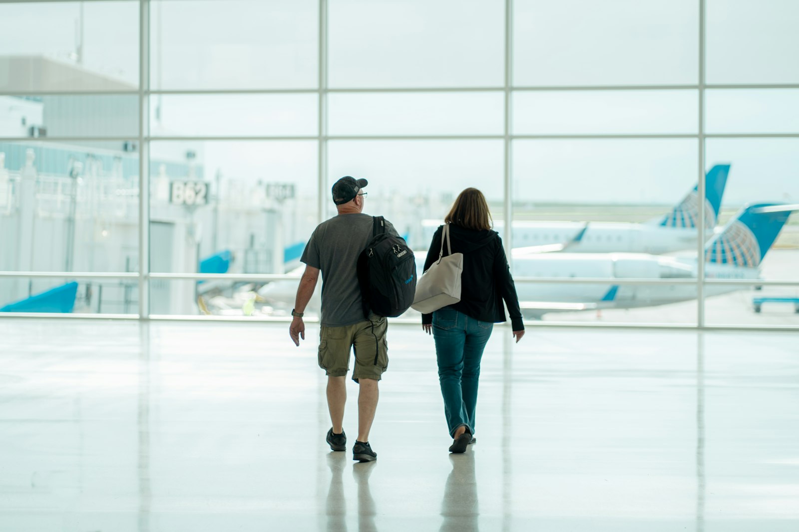 Casal caminhando pelo aeroporto puxando malas, prontos para embarcar num feriado prolongado