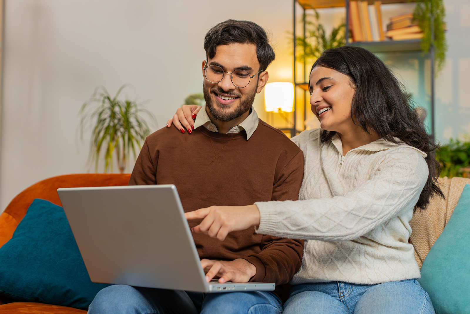 Casal sorridente comparando opções de viagem no notebook em casa