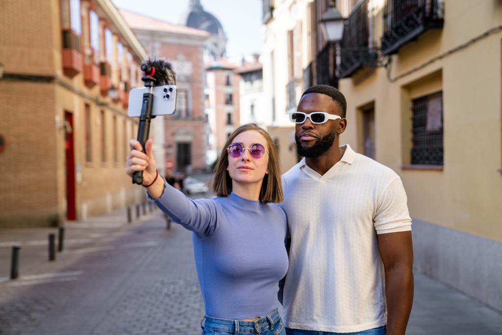 Dois criadores de conteúdo gravando vídeo vertical com celular e bastão de selfie em uma rua histórica