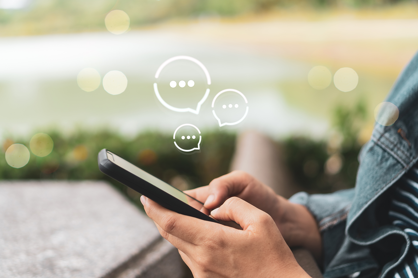 Mão segurando um celular com ícones de balões de conversa, representando mensagens diretas