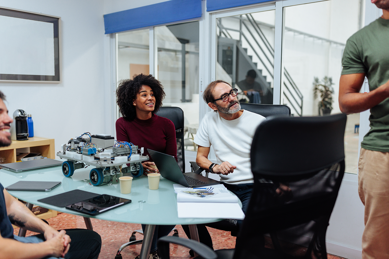 Grupo de pessoas reunidas ao redor de uma mesa em escritório testando um protótipo de equipamento sobre a mesa