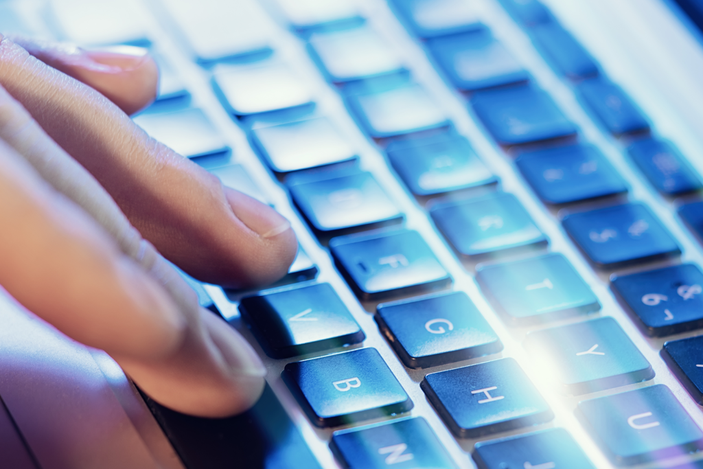 Mãos digitando em teclado de notebook com luz azul, representando busca digital assistida por IA