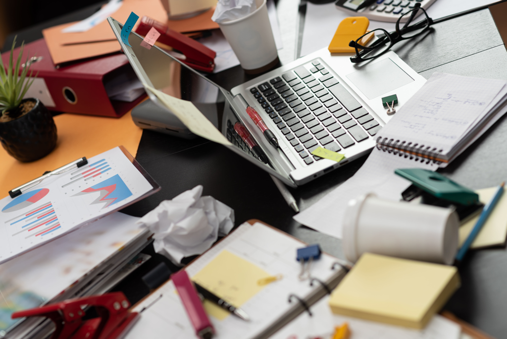 Mesa de escritório desorganizada com laptop, planilhas impressas e anotações soltas, representando a bagunça de leads sem CRM