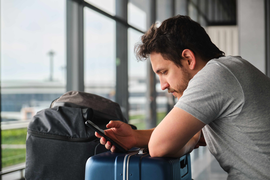 Viajante corporativo sentado no aeroporto fazendo check-in e gestão da viagem pelo smartphone