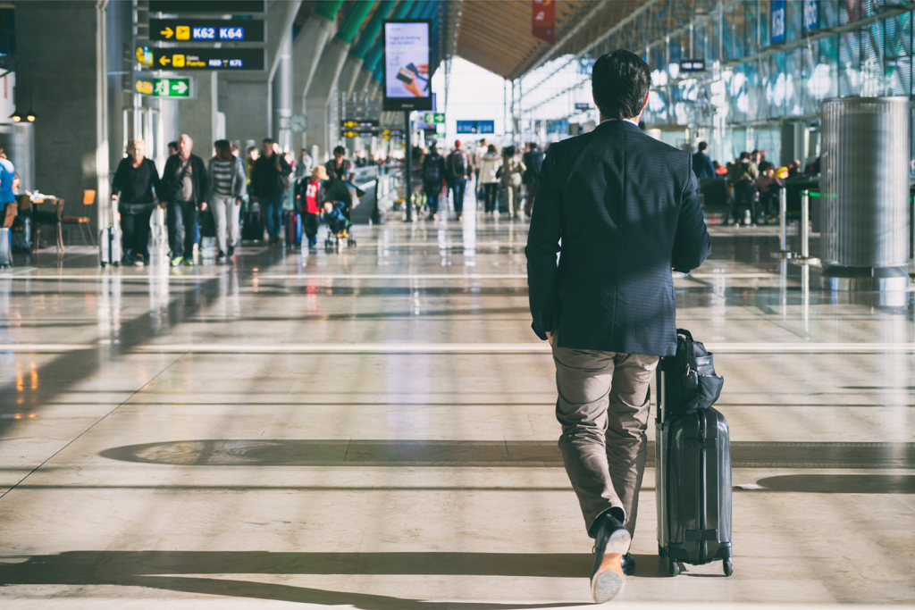 Homem de terno caminhando com mala de rodinhas em terminal de aeroporto movimentado