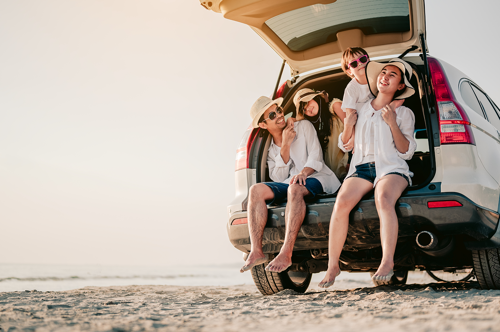 Família sentada no porta-malas do carro na praia, mostrando viagem doméstica de carro