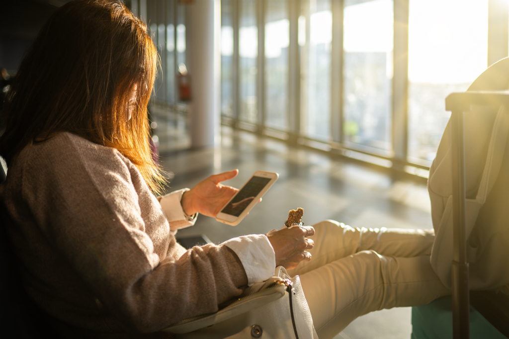 Mulher sentada com bagagem no saguão do aeroporto usando o celular para trocar mensagens