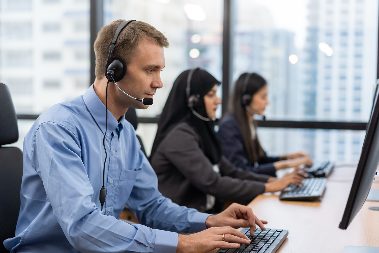 Equipe de atendimento com headset trabalhando em computadores em central de atendimento