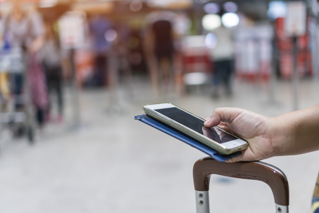Mão segurando smartphone sobre mala de viagem em aeroporto, fazendo check-in digital