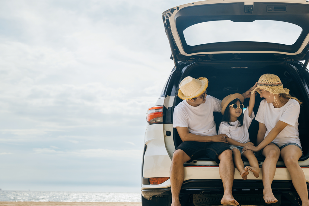 Família sentada no porta-malas do carro em frente à praia durante viagem doméstica